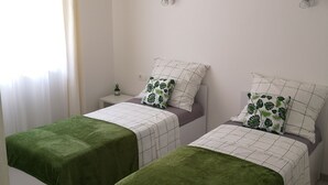 Un dormitorio con dos camas individuales, cada una con una manta verde y un cojín blanco estampado con hojas.