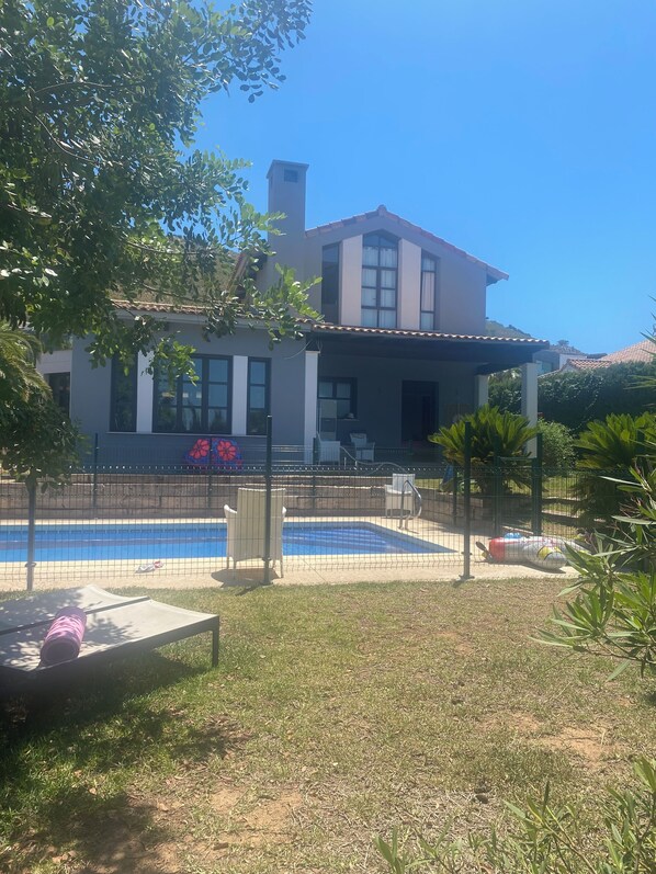 Uma casa de dois andares com piscina, varanda coberta e quintal cercado.