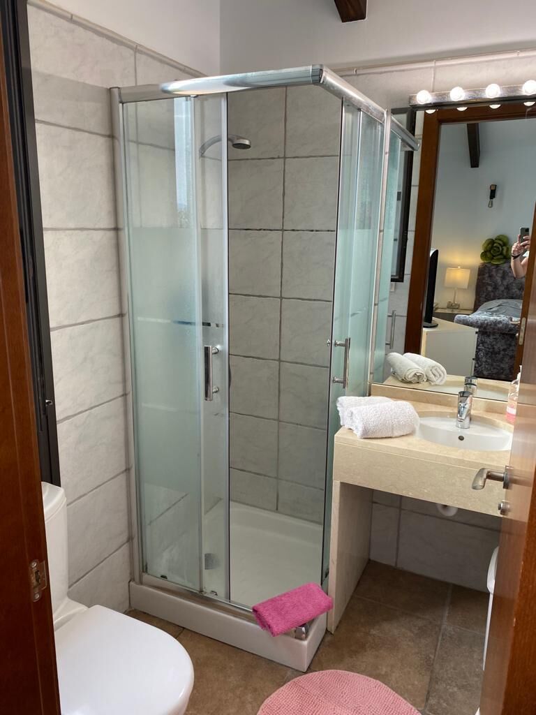 A modern bathroom with a glass-enclosed shower, a white toilet, a sink with a mirror, and a pink towel on the floor.
