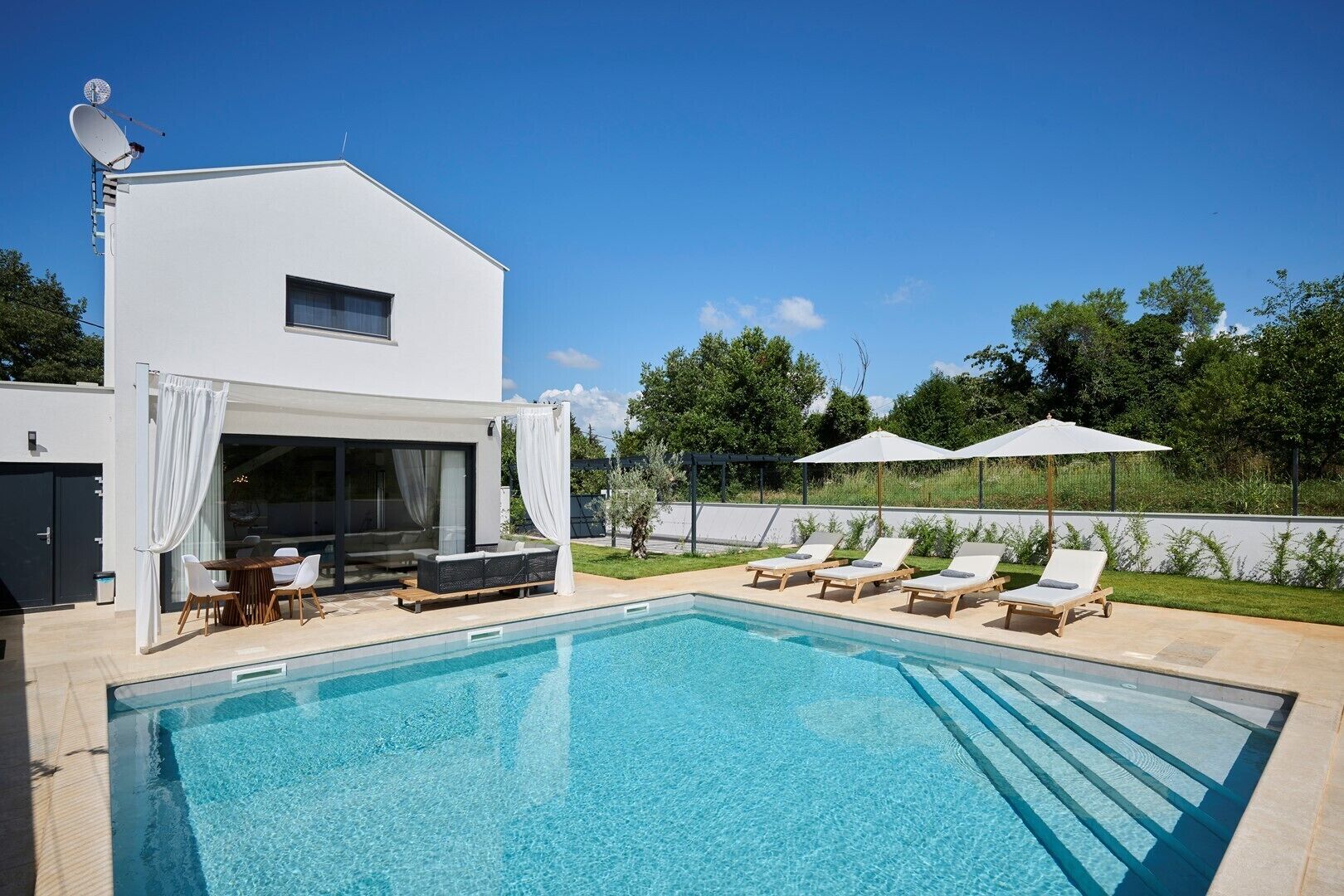 Una casa moderna con piscina, mobiliario exterior y un porche cubierto.