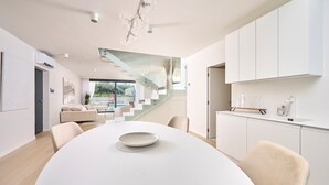 A modern kitchen with white cabinetry, a dining area with a round table, and a staircase leading to an upper level.