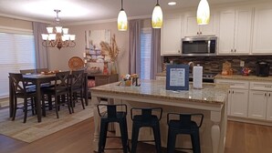 A modern kitchen with a central island, bar stools, a chandelier, and a welcome sign.