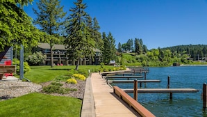A lakeside walkway with docks, a grassy area, and a building with a balcony.