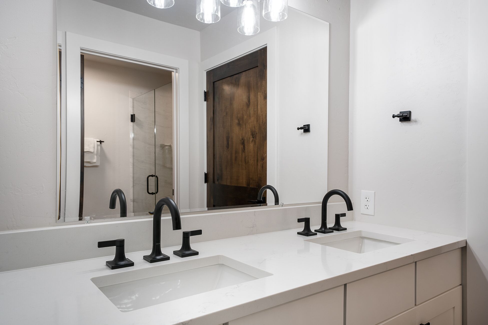 Un baño moderno con dos lavamanos, un espejo grande y una puerta de madera.