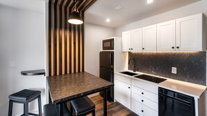 A compact kitchen with white cabinets, a black refrigerator, a microwave, a sink, and a dining area with a table and two stools.