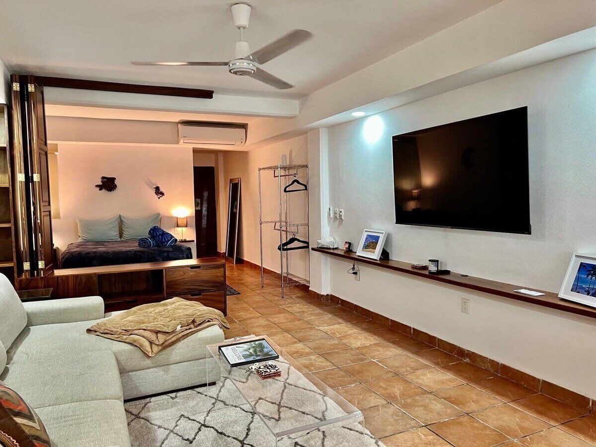Una sala de estar moderna con un sofá, una mesa de centro, un televisor montado en la pared y un ventilador de techo.