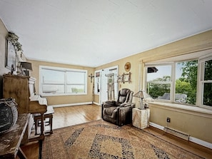 A spacious living room with a large window, a leather armchair, a wooden cabinet, and a patterned rug.