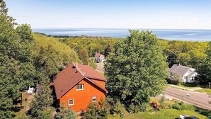 A red house with a sloped roof surrounded by lush greenery and a view of the sea.