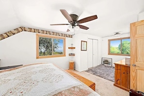 A bedroom with a bed, a ceiling fan, a window, a door, and a cabinet.