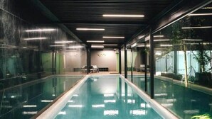 Ein modernes Hallenbad mit großen Glaswänden, minimalistischem Design und einer Sitzecke mit Tisch und Stühlen.