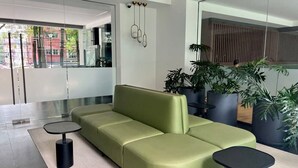 Eine moderne Lobby mit einem grünen Sofa, zwei schwarzen Beistelltischen und Topfpflanzen.