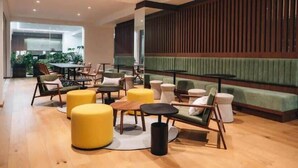 Ein moderner Lounge-Bereich mit Holzboden, gelben Hocker und grünen Polstersitzmöglichkeiten.