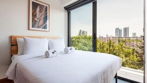 Ein Hotelzimmer mit einem großen Bett, Blick auf die Stadt durch eine Schiebetür und einem gerahmten Bild an der Wand.