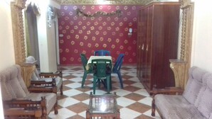 A living room with a checkered floor, two armchairs, a small table, a dining table with chairs, and a red patterned wall. - A 3-BR apt w FP, GV & 20 min to the sea & Muntazah (Al Mandarah Qebli, Montaza 2)
