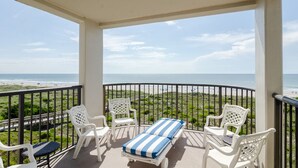 A balcony with white chairs and a striped cushion, overlooking a beach with a clear view of the ocean. - Stunning oceanfront end unit in Duneridge! (Wrightsville Beach)