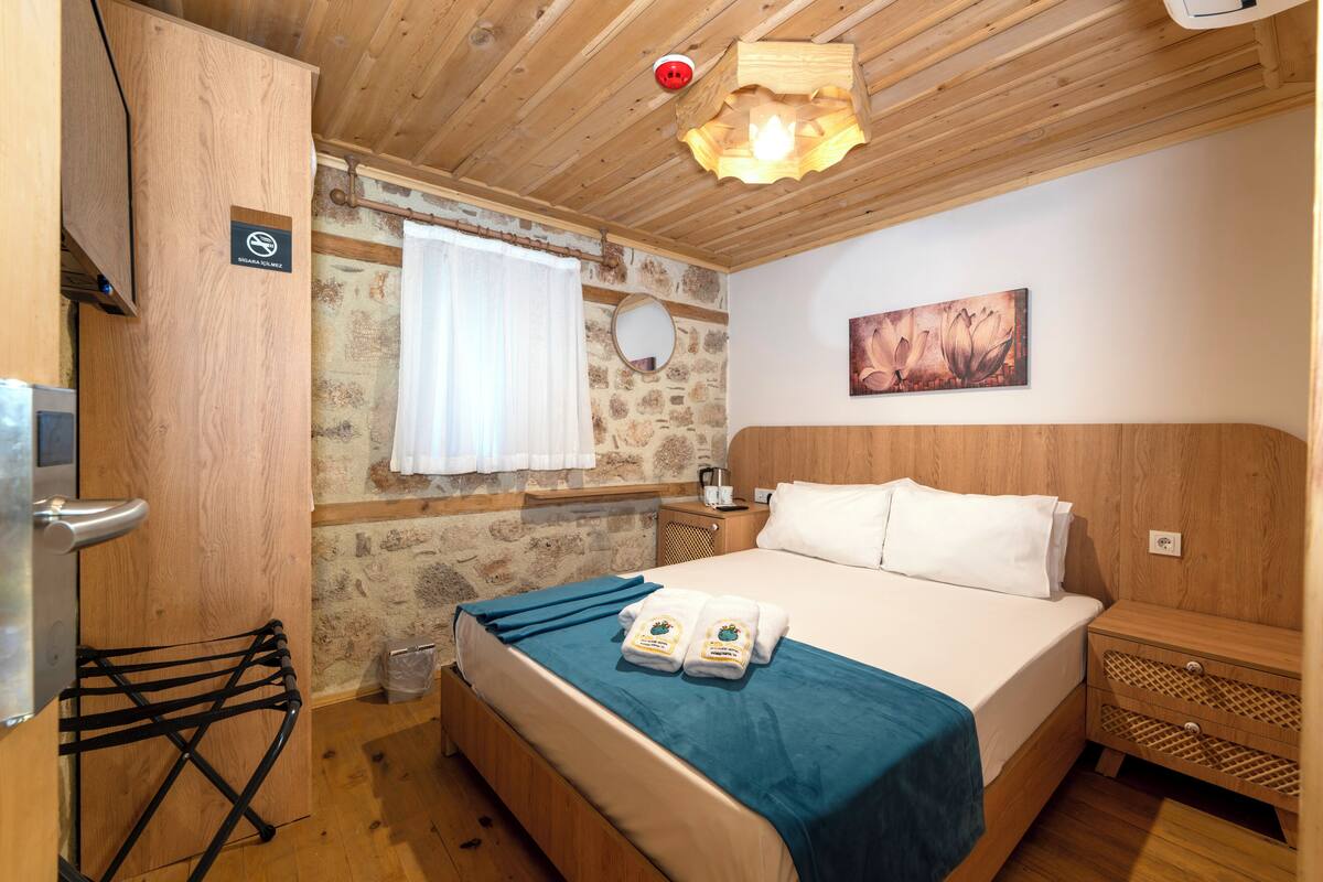 Una stanza con rivestimenti in legno, un letto, un comodino in legno, un porta asciugamani e una parete in pietra.