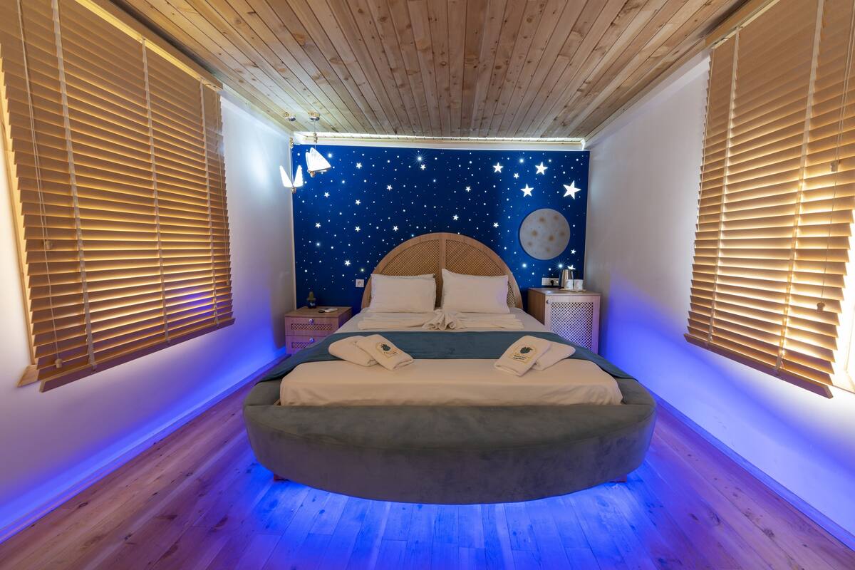 Camera da letto con un affresco raffigurante una notte stellata, un letto rotondo con testiera in legno e persiane di legno alle finestre.