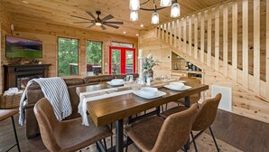 A wooden interior with a dining area, sofa, fireplace, TV, and a staircase. - 4King Suites | Hot Tub | Game Room | Sunrise Views (Gatlinburg)
