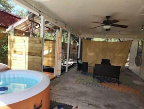 Relax in a serene outdoor space with a hot tub, seating, and a ceiling fan, surrounded by a fence.
