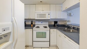 Una cocina compacta con armarios blancos, un microondas integrado, una estufa y un lavamanos.