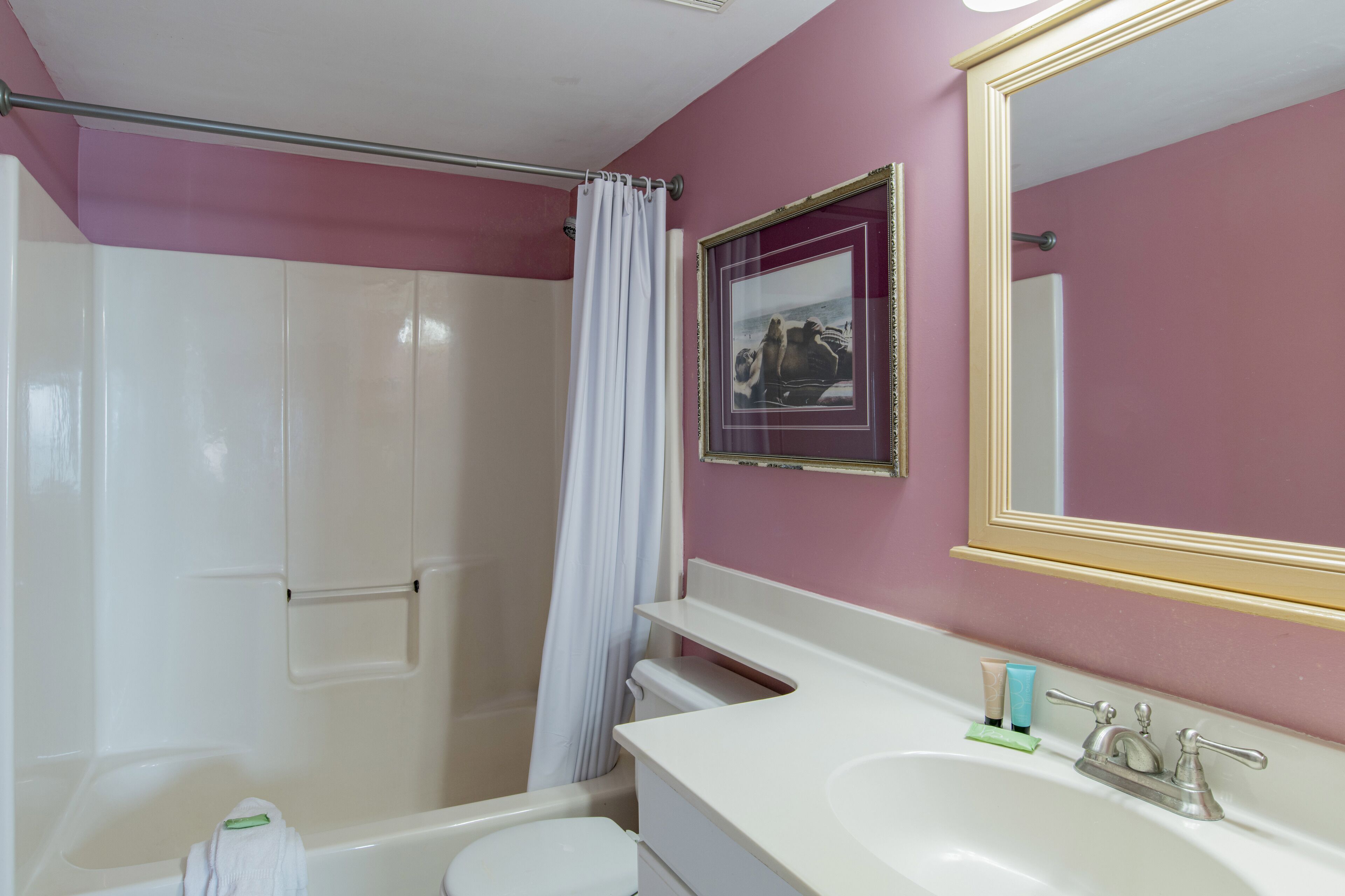 A bathroom with a shower, toilet, sink, and a mirror.