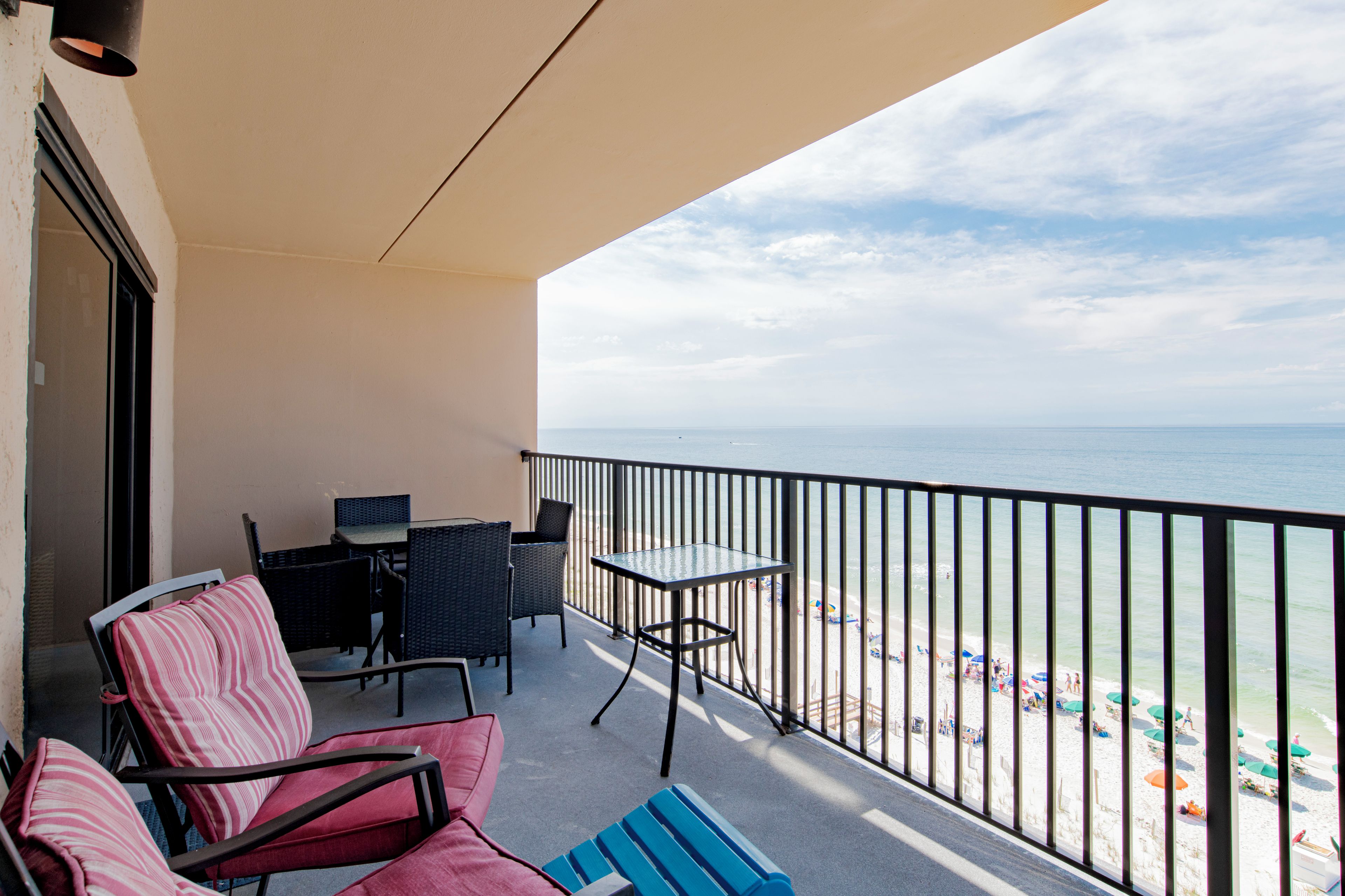 Een balkon met uitzicht op het strand, met een tafel, stoelen en een kleine bank.