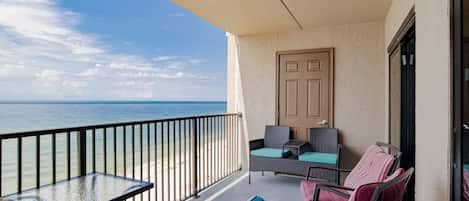 A balcony with a glass table and chairs, a door, and a view of the ocean.