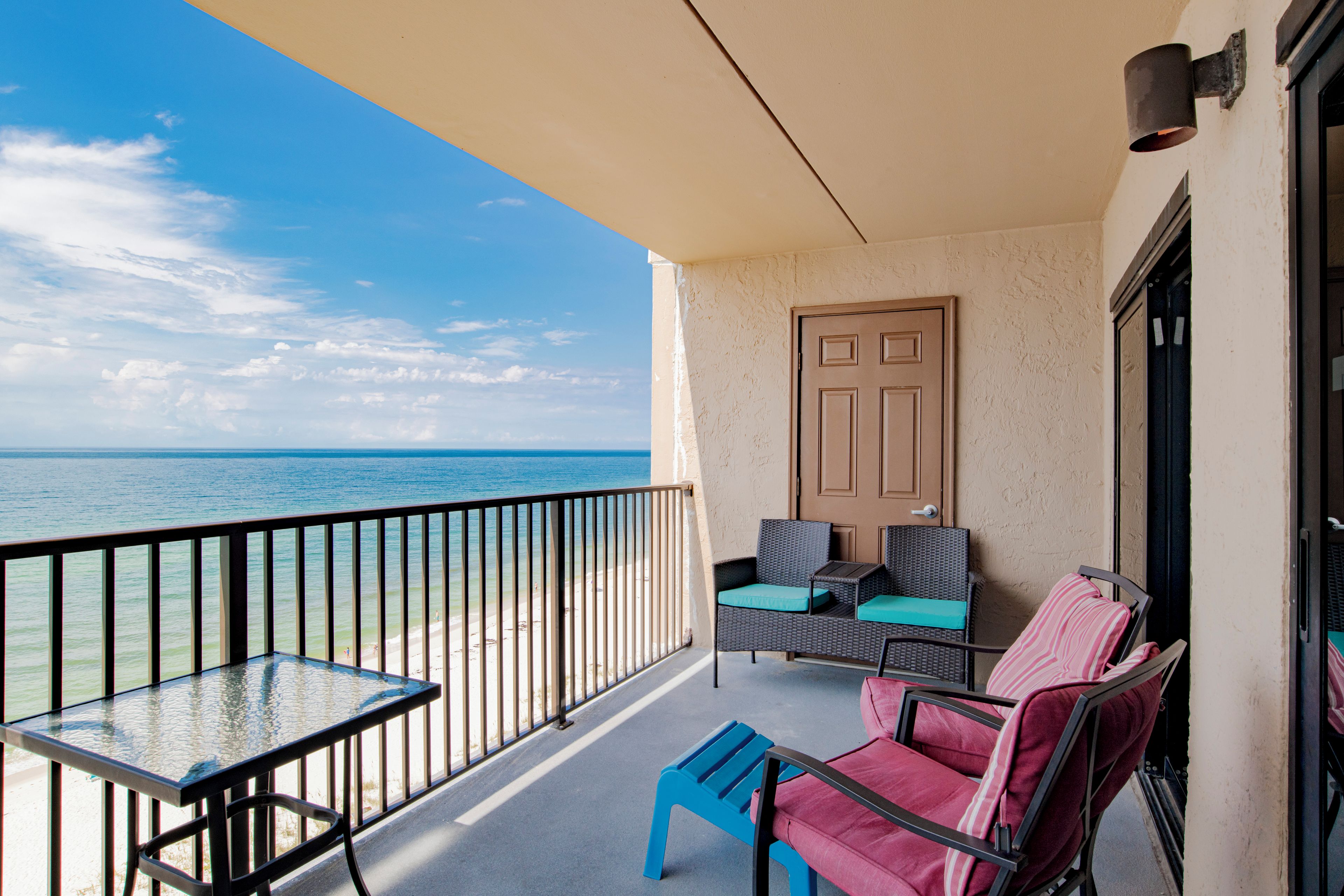Een balkon met een glazen tafel en stoelen, een deur en uitzicht op de oceaan.