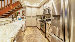Una cocina moderna con electrodomésticos de acero inoxidable, escalera de madera y encimeras de mármol.