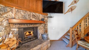 Una chimenea de piedra con un televisor montado encima, una escalera de madera y un cesto de leña.