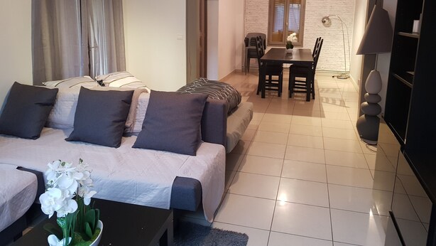 Una sala de estar moderna con sofá, una mesa de comedor con sillas, televisor y lámpara.