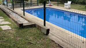 Une piscine entourée d’une clôture, avec une pelouse et des arbres en arrière-plan.