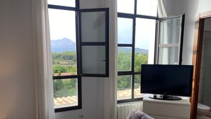 Une chambre à coucher avec un lit, un téléviseur posé sur un meuble et une fenêtre donnant sur un paysage verdoyant et montagneux.