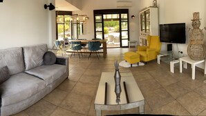 Un salon avec un canapé gris, une table basse en verre, un fauteuil jaune et un téléviseur posé sur un meuble blanc.