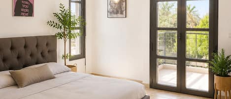 A bedroom with a large bed, a ceiling fan, a wall-mounted air conditioner, and a sliding glass door leading to a balcony.