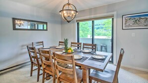 A dining area with a wooden table set for six, a chandelier, and a large window with a view of greenery. - Cozy Lincoln Condo ~ 1 Mi to Loon Mountain! (Lincoln)