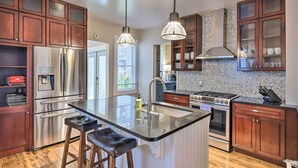A modern kitchen with stainless steel appliances, wooden cabinets, and a central island with bar stools. - Milwaukee Home < Half Mi to Lake Michigan! (Milwaukee)