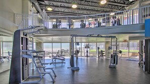 Ein mehrgeschossiges Fitnessstudio mit unterschiedlichen Trainingsgeräten, einer erhöhten Zwischenebene mit Geländer und großen Fenstern für natürliches Licht.