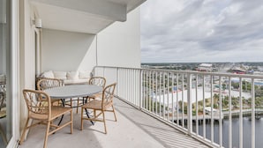 Ein Balkon mit rundem Tisch und vier Korbstühlen, mit Blick auf eine Stadtlandschaft mit Wasseroberfläche und Gebäuden.