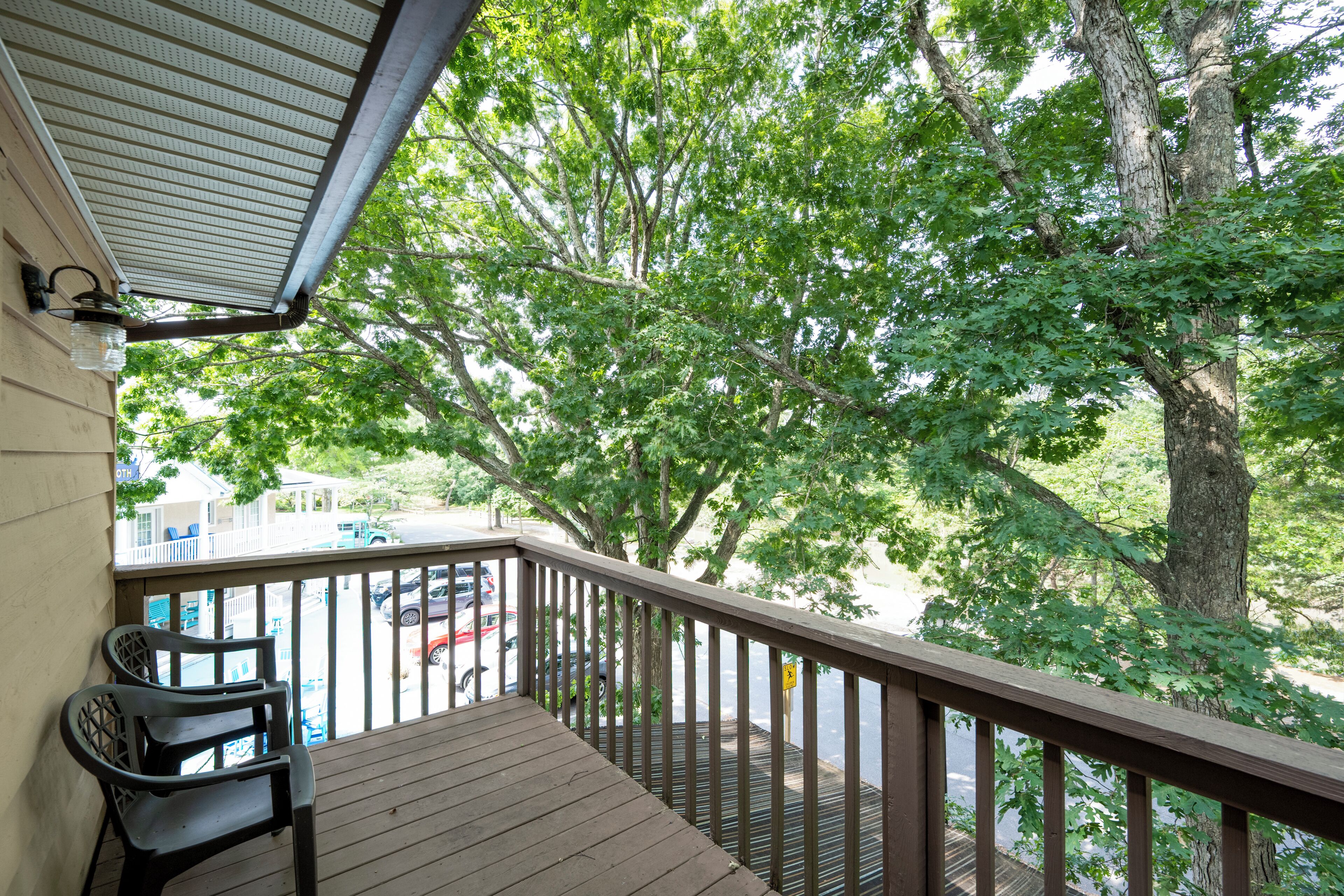 A wooden deck with a railing overlooking a parking area and trees.