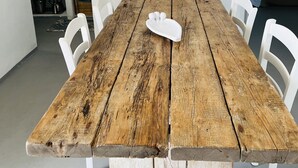 Een rustieke houten eettafel met witte stoelen, een witte keramieken schaal en een keuken met tegels en keukengerei.