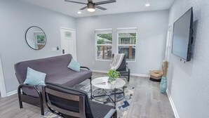 Un salon moderne avec un canapé, des fauteuils, une table basse et un téléviseur fixé au mur.