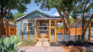 Une maison dotée d’un porche abrité, d’une clôture en métal et d’un jardin où poussent différentes espèces de plantes.