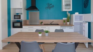 A modern kitchen with teal walls, white cabinetry, a wooden dining table, and a black range hood.