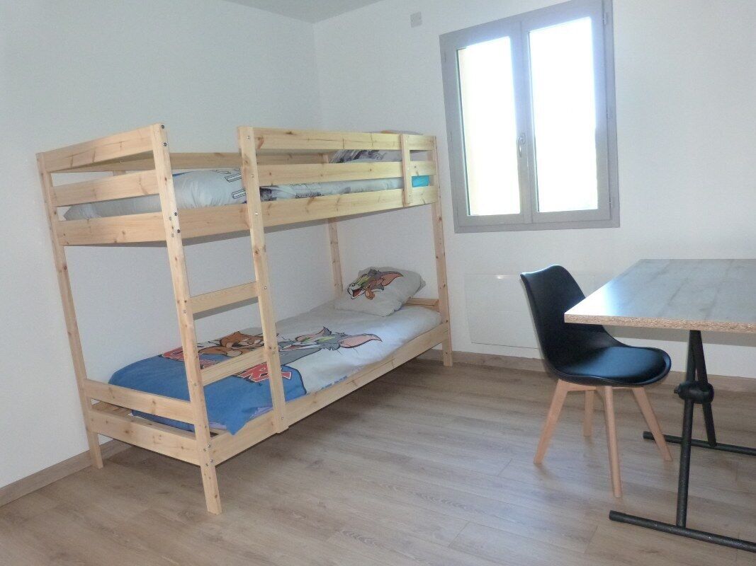 Una cama individual en literas con escritorio y silla, una ventana y piso de madera.