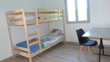 Una cama individual en literas con escritorio y silla, una ventana y piso de madera.