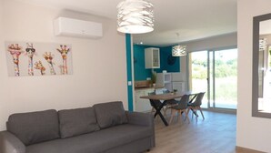 A modern living room with a grey sofa, a dining area with a table and chairs, and a kitchen in the background.