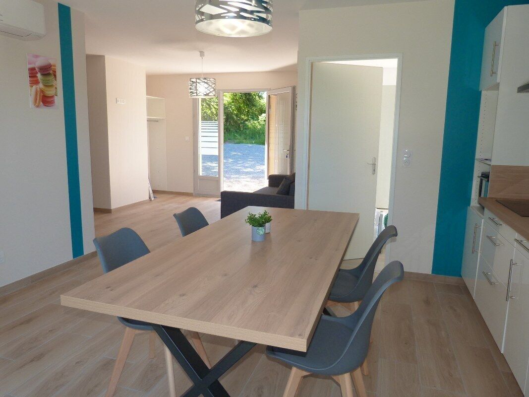 Un comedor moderno con una mesa y sillas de madera, una planta pequeña sobre la mesa, y vistas al exterior a través de un ventanal.