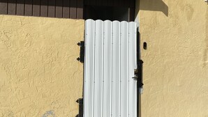 A corrugated metal gate attached to a textured yellow wall with a brown roof above. - Beautiful 2 bedroom house walking distance from hard rock stadium (Miami Gardens)