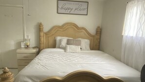 A neatly made bed with a wooden headboard, a bedside table with a lamp, and a framed sign on the wall. - Beautiful 2 bedroom house walking distance from hard rock stadium (Miami Gardens)
